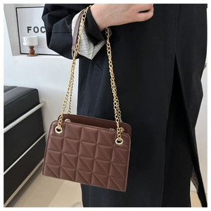 Detail of a brown quilted leather crossbody bag with elegant gold chain strap worn by a model