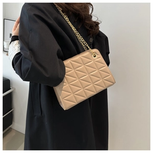 Close-up of beige quilted crossbody bag with golden chain strap on a person