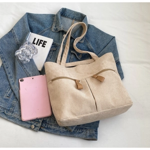 Detail view of beige corduroy tote bag with front zip pockets on denim background