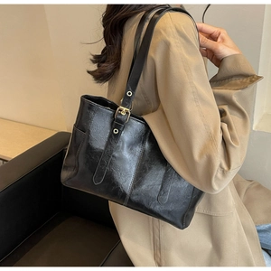 Close-up of black glossy leather tote bag showing metal buckle detail on shoulder strap