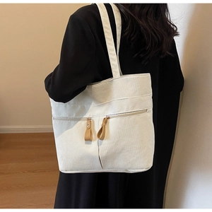 Detailed back view of a white corduroy tote bag worn by a model in a warm indoor setting