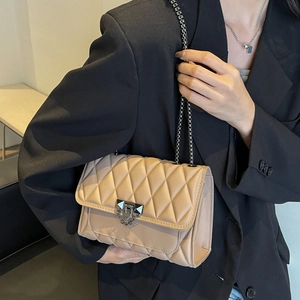 Elegant beige quilted chain shoulder bag with metal clasp worn with a black suit