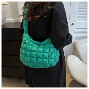 Detail view of a bright green quilted puffer hobo bag worn with a black wool coat