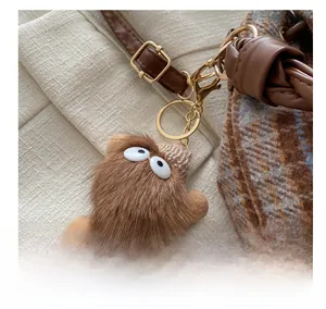 Detailed close-up of a brown fuzzy monster charm with knitted hat on a plaid bucket bag