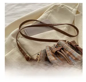 Detail showing wool plaid bucket bag with brown leather strap and woven handle texture