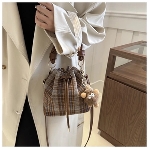 Detail of plaid bucket bag with drawstring closure and cute plush monster pendant