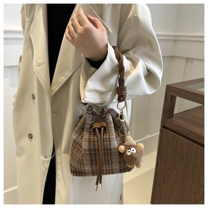 Close-up of vintage plaid bucket bag with braided handle and plush monster charm