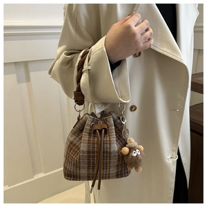 Detail view of plaid wool bucket bag with woven handle and plush bear charm