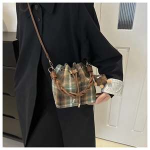 Detail of plaid wool bucket bag with woven handle and plush charm on a black coat