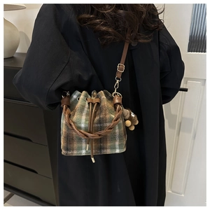 Detail of plaid wool bucket bag with drawstring closure and brown plush bear charm
