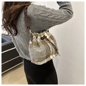 Detailed close-up of plaid wool bucket bag with drawstring closure and leather strap