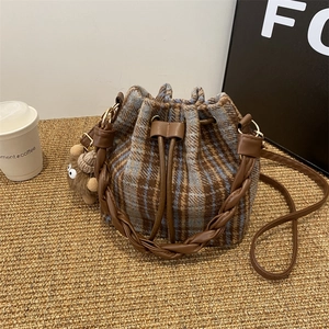 Detail of plaid wool bucket bag with leather woven handle and cute plush charm on base