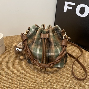 Detail of checkered tweed bucket bag featuring leather drawstring and plush monster charm