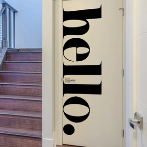 Close-up of a minimalist black vinyl 'hello.' sticker applied to a white wooden door