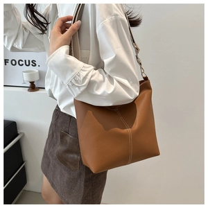 Detail of caramel leather bucket bag with white contrast stitching and canvas strap