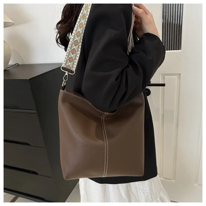 Detail of dark brown leather bucket bag with white stitching and textured wide strap