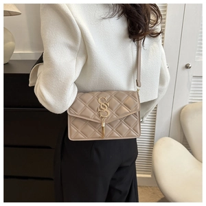 Detail der beigen Stepptasche mit goldenen Beschlägen und metallischen Quastenakzenten