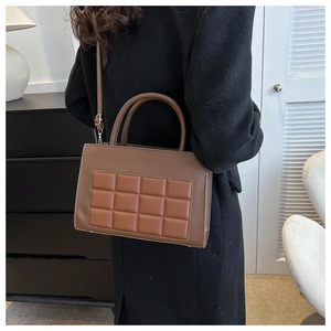 Detail of caramel brown quilted crossbody bag shown with black wool coat on model