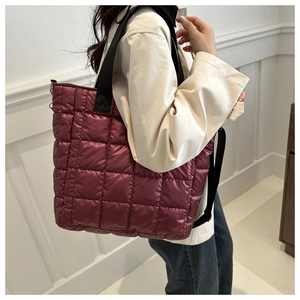 Detalle de bolso tote acolchado burdeos con bandolera negra usado por el modelo en foto