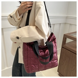 Detalle de bolso tote acolchado burdeos metalizado llevado sobre una gabardina beige