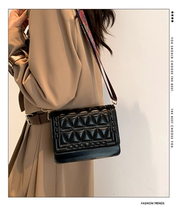 Detail of black quilted crossbody bag featuring a colorful geometric woven wide strap
