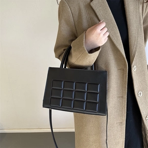 Women's black quilted rectangular handbag with adjustable strap shown with a winter coat