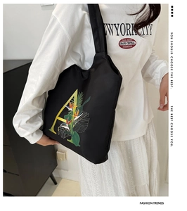 Détail d'un sac cabas noir avec une lettre A jaune et un imprimé oiseau du paradis