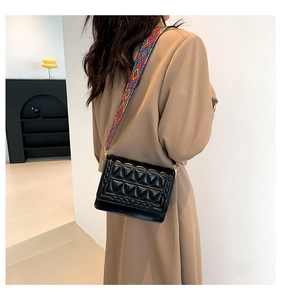 Detail of black quilted crossbody bag with textured geometric flap and wide embroidered strap