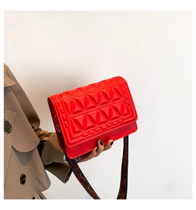 Detail of red quilted square bag with ethnic geometric woven wide strap on trench coat