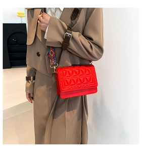 Close-up of vibrant red leather crossbody bag with colorful geometric woven wide strap