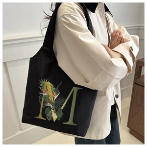 Détail du sac cabas en toile noire avec lettre M et motif floral de fleurs tropicales