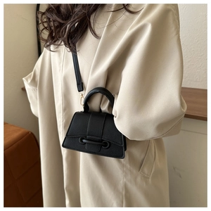 Détail du mini sac en cuir noir à texture litchi porté sur un trench-coat beige élégant
