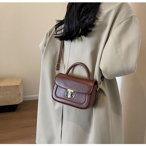 Modella che indossa una borsa a tracolla marrone scuro con chiusura a rotazione dorata