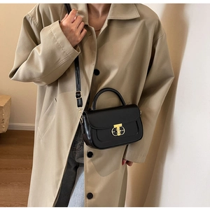 Dettaglio di una borsa in pelle nera con chiusura a T dorata indossata con un trench classico