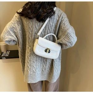 Piccola borsa quadrata bianca in pelle con chiusura dorata su un maglione a maglia