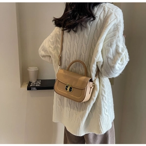 Dettaglio di una borsa beige con chiusura metallica a T indossata su un maglione bianco