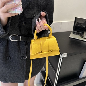 Mini sac à main en cuir grainé jaune vif avec bandoulière sur un manteau d'hiver gris