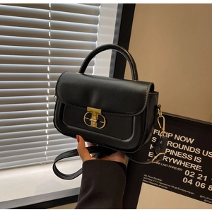 Dettaglio borsa in pelle nera con chiusura geometrica dorata e tracolla regolabile