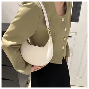Sac hobo blanc cassé avec boucles dorées porté par un mannequin en veste verte chic