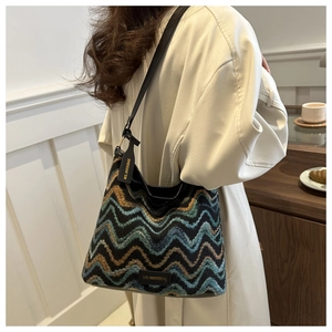 Close-up of zigzag patterned tweed tote bag with slim black strap on beige coat