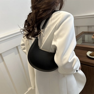 Sac hobo minimaliste en cuir noir mat avec boucles dorées porté par un mannequin en blanc