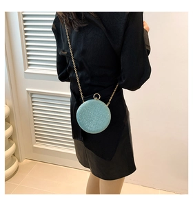 Sparkling light blue ball evening bag with gold chain strap worn cross-body on black dress
