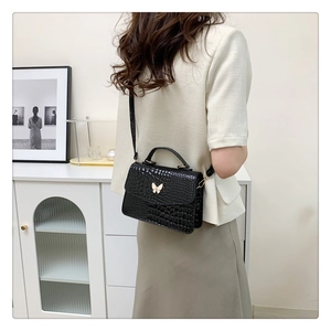 Detail of black crocodile texture bag with elegant gold butterfly clasp and adjustable strap