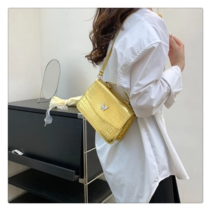 Close-up of golden crocodile embossed shoulder bag with a silver butterfly clasp
