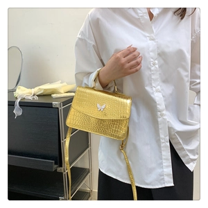 Close-up of golden metallic handbag with crocodile texture and white butterfly buckle