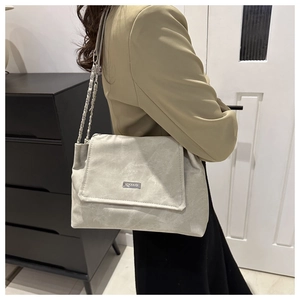Detail of light gray faux suede shoulder bag with chain strap worn by a female model