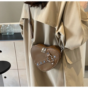 Sac bandoulière marron en forme de cœur avec rivets porté sur un trench-coat beige