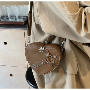 Détail d'un sac bandoulière marron en forme de cœur avec rivets et sangle réglable