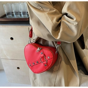 Détail du sac à main rouge en forme de cœur avec rivets sur un trench-coat beige