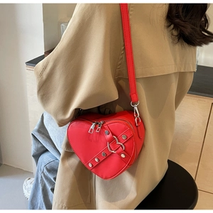 Détail du sac à bandoulière rouge en forme de cœur avec boucle et clous argentés